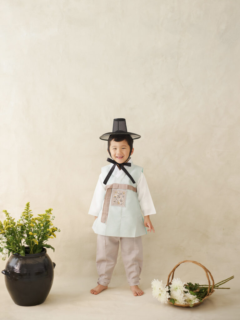 Chicago dol portrait of child standing in white hanbok beside a floral arrangement in a minimal studio