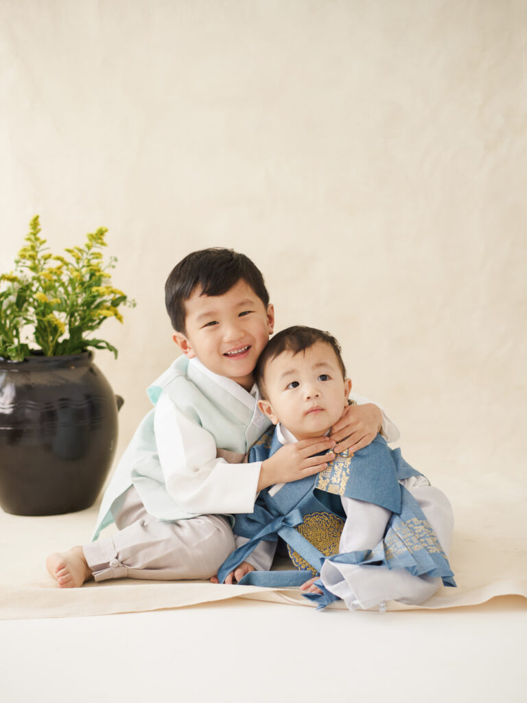 Chicago dol sibling photo with two children sitting close together in soft toned outfits in a calm studio space