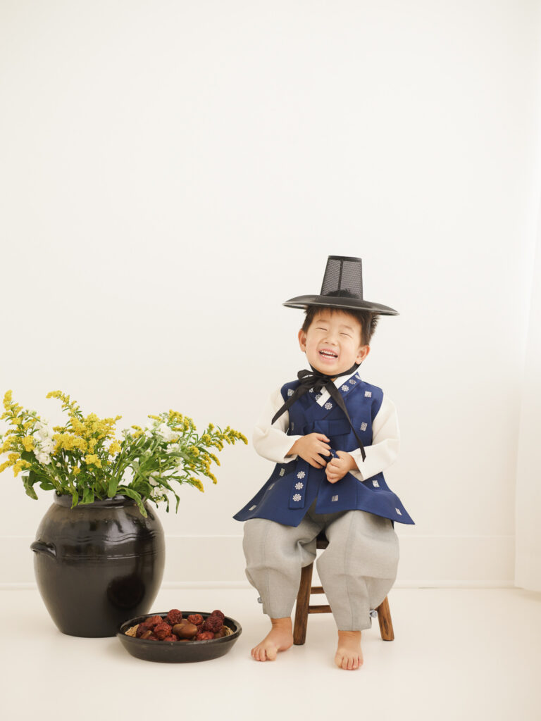 Chicago dol portrait of young child in blue hanbok and traditional hat sitting on a small wooden chair