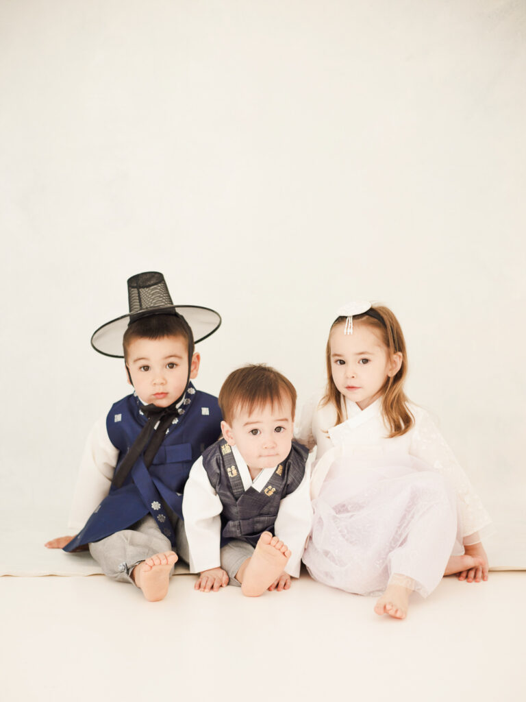 Chicago dol photographer capturing three children in traditional Korean outfits sitting together in a bright studio