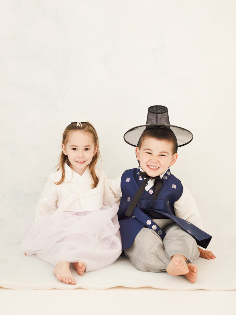 Chicago dol family session with siblings in coordinated hanbok outfits sitting side by side on a clean backdrop