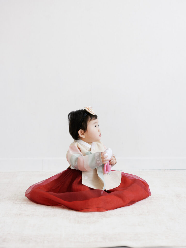 Chicago dol first birthday photography of baby girl in traditional hanbok sitting on a red mat in a minimal studio