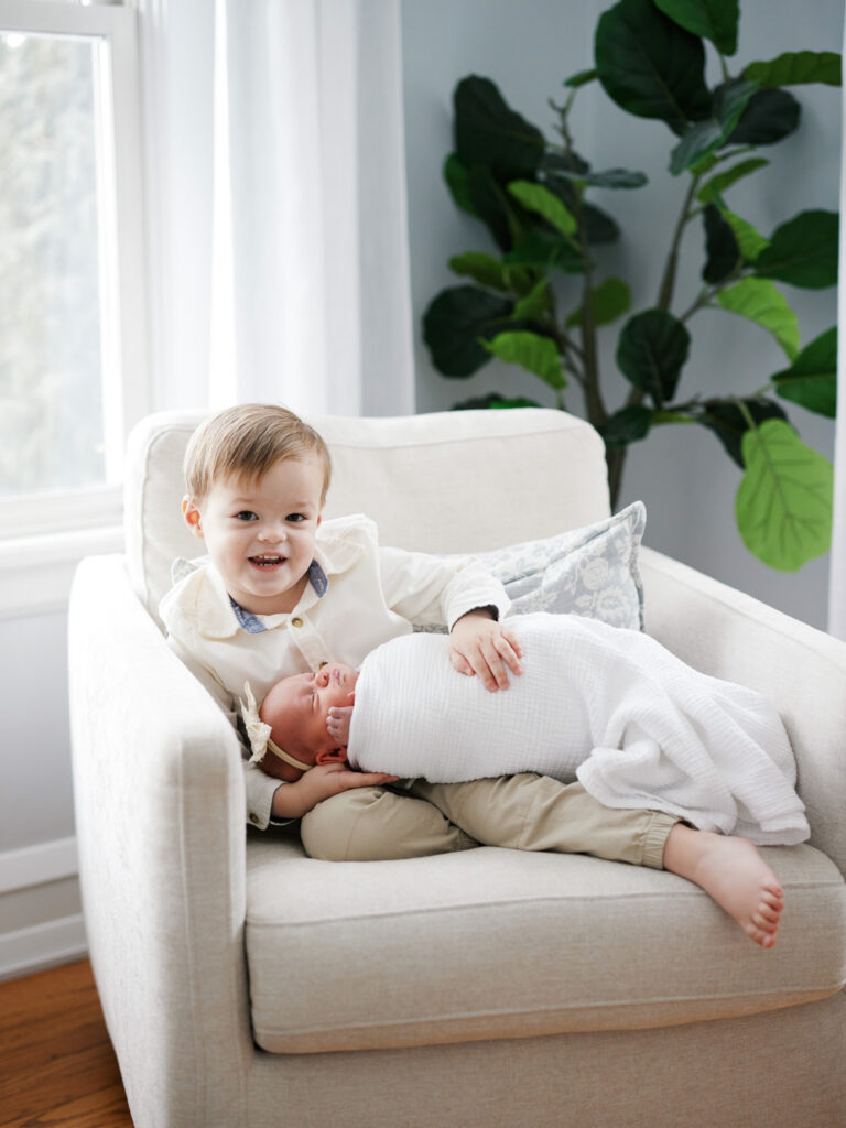 Toddler sibling lying next to sleeping newborn baby on cream sofa during in-home newborn session in Western Springs Illinois