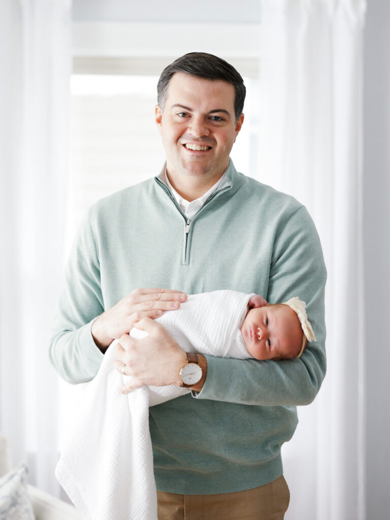 Smiling father holding swaddled newborn baby during in-home newborn photography session in Western Springs Illinois