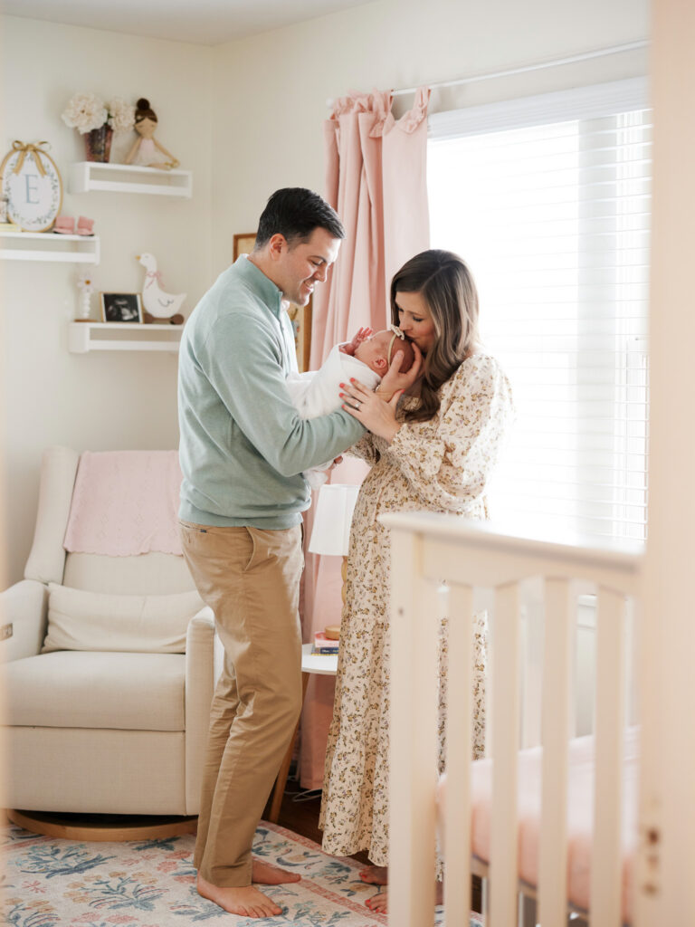 Parents leaning over blush nursery crib with newborn during in-home session in Western Springs IL